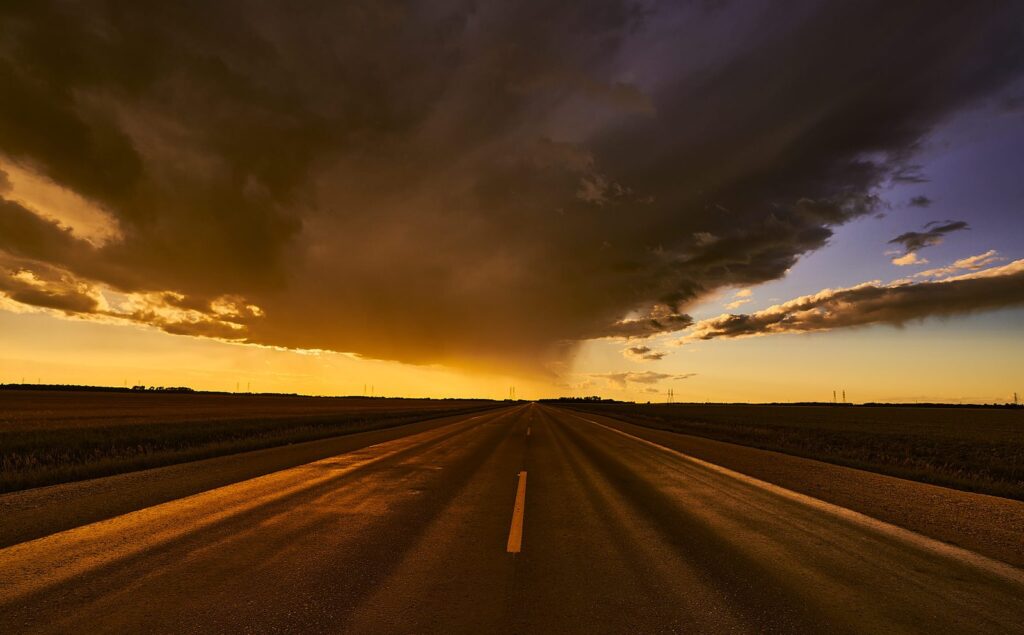Golden light under a dark storm cloud over a straight highway