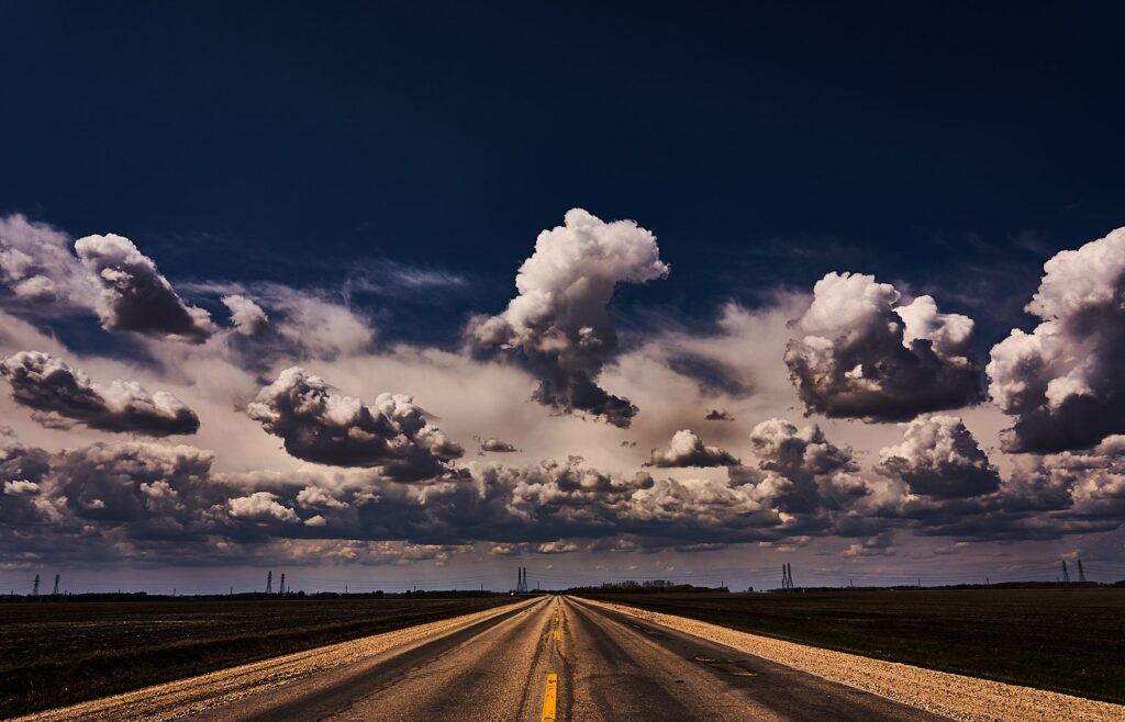 White cumulus clouds over a gravel road under a deep blue sky