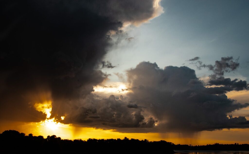 Dark storm cloud with sunlight bursting through at the edge and rain below