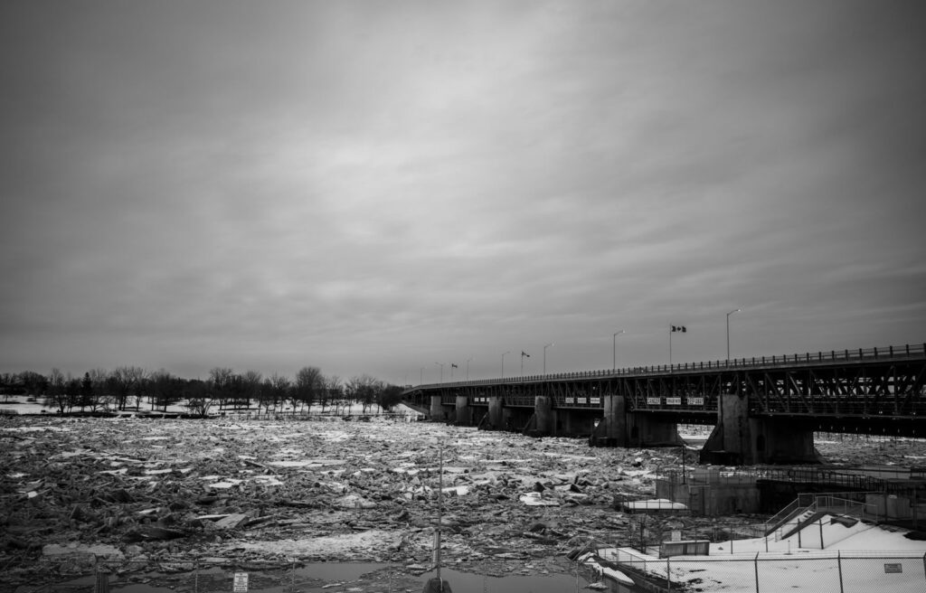 Ice-choked river beneath a long steel bridge under a heavy sky