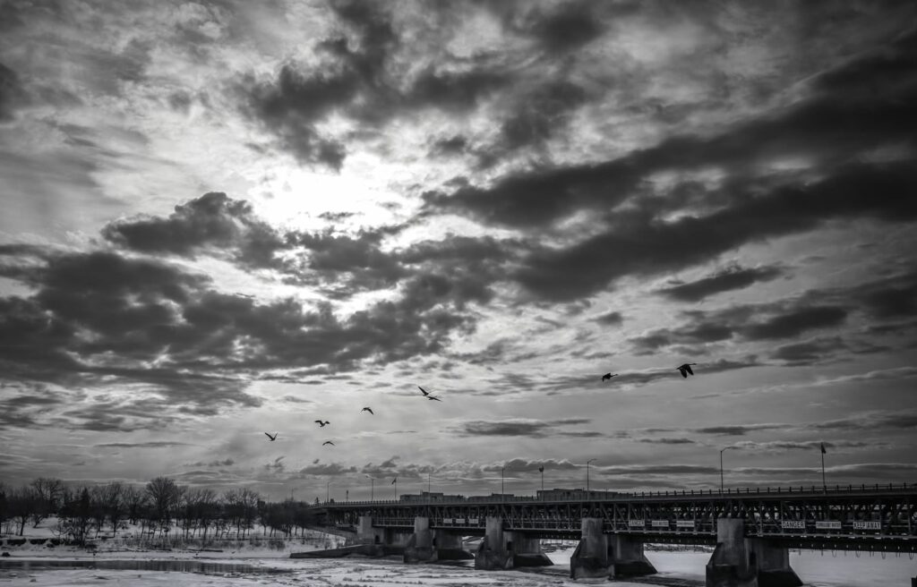Dramatic clouds and a flock of geese over a bridge and river