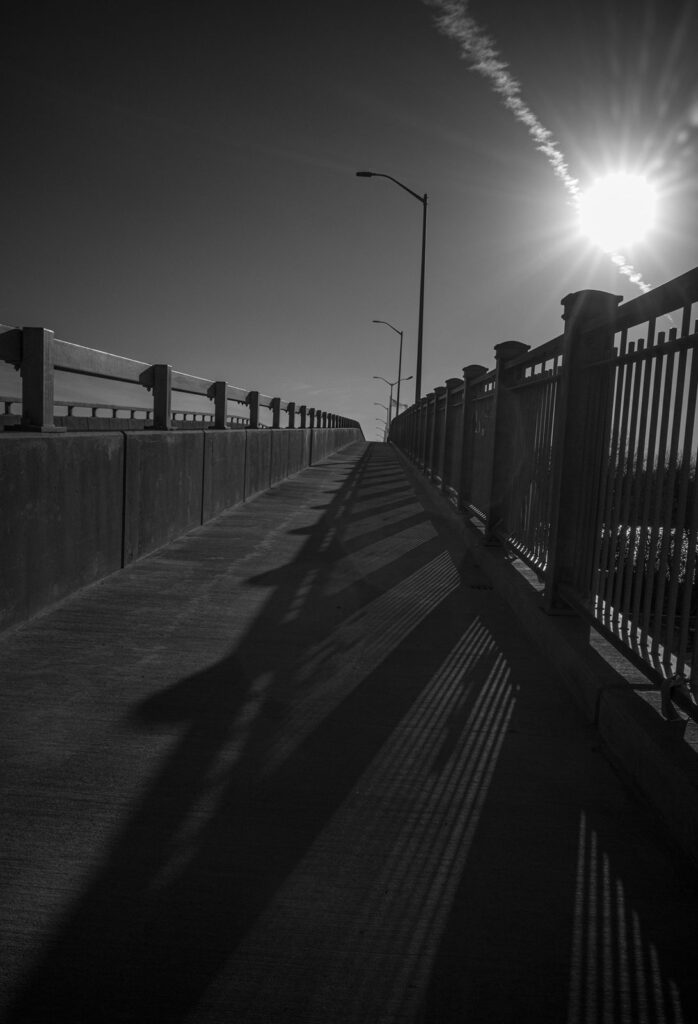 Bridge walkway with a railing, long shadows, and a bright low sun