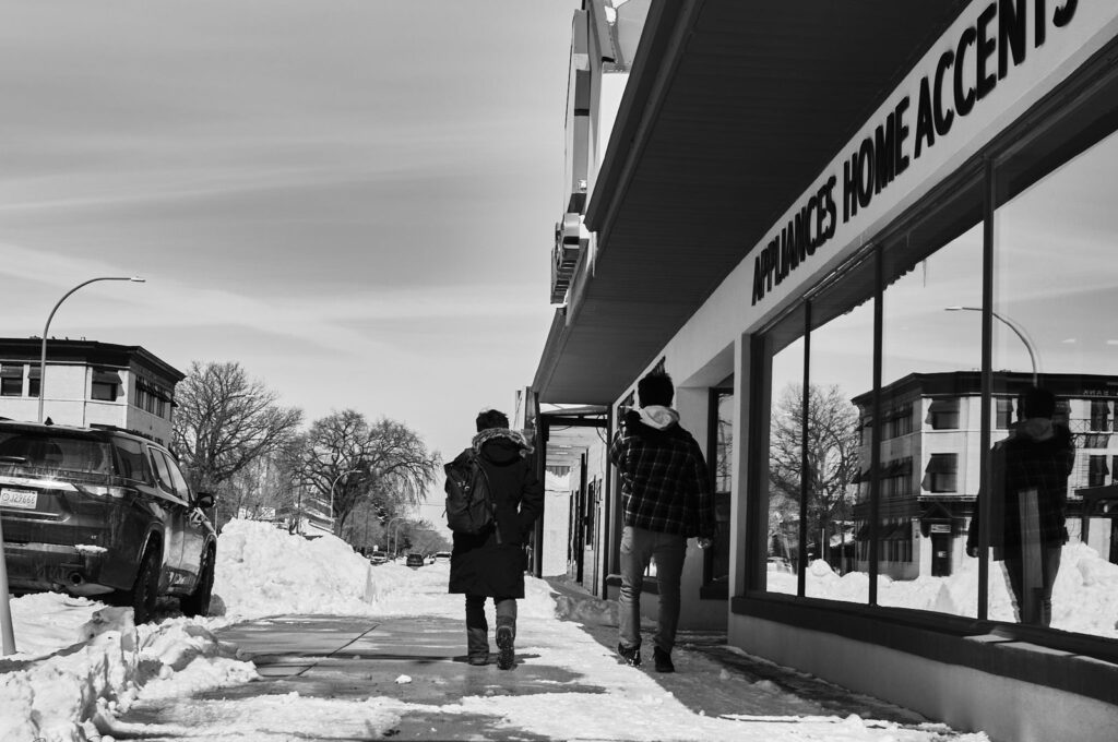 People walking along a snowy sidewalk past a storefront window