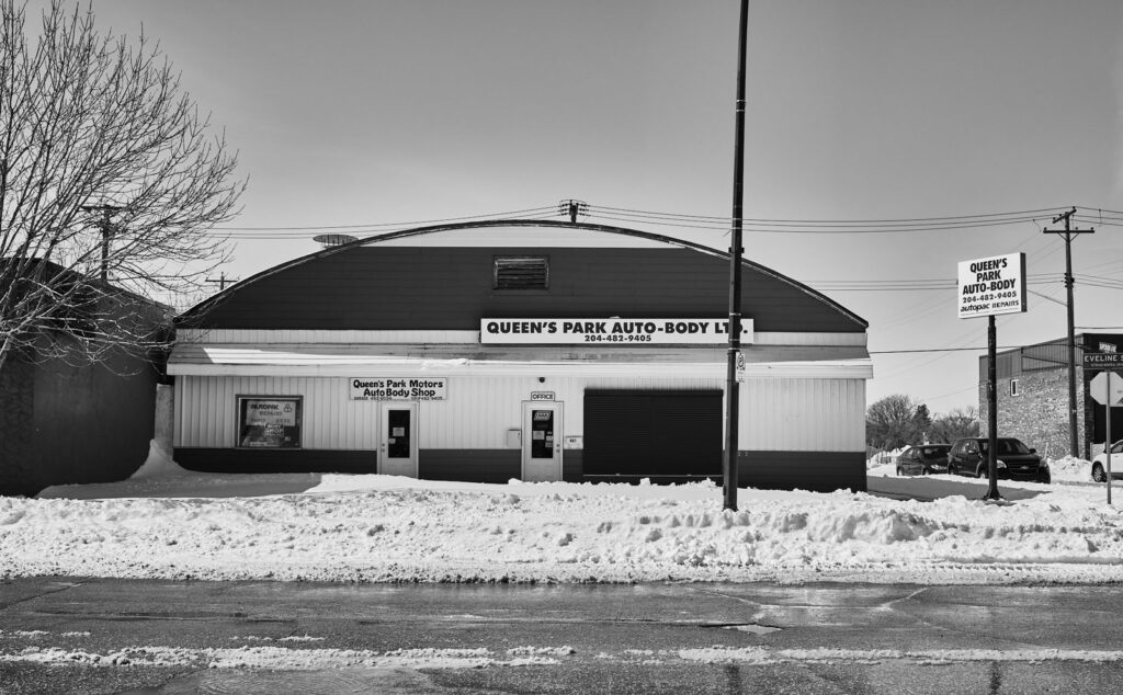 Auto body shop with a curved roof beside a snowbank on a winter day