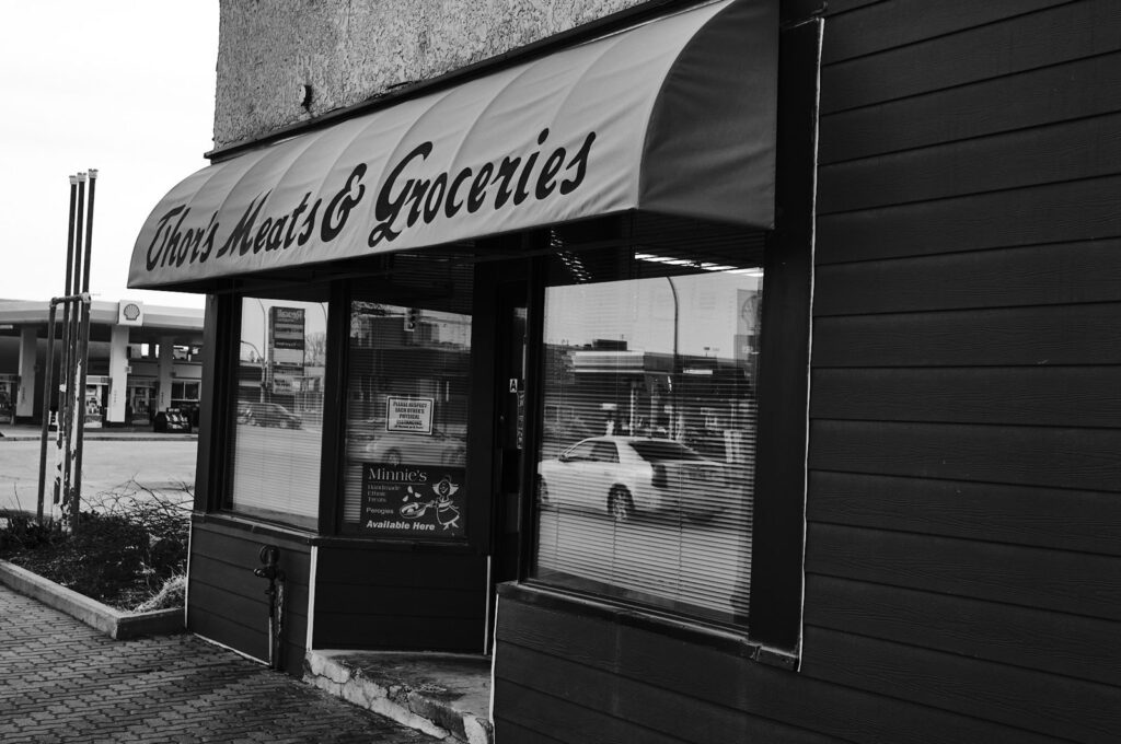 Corner grocery with a striped awning and a car reflected in its window