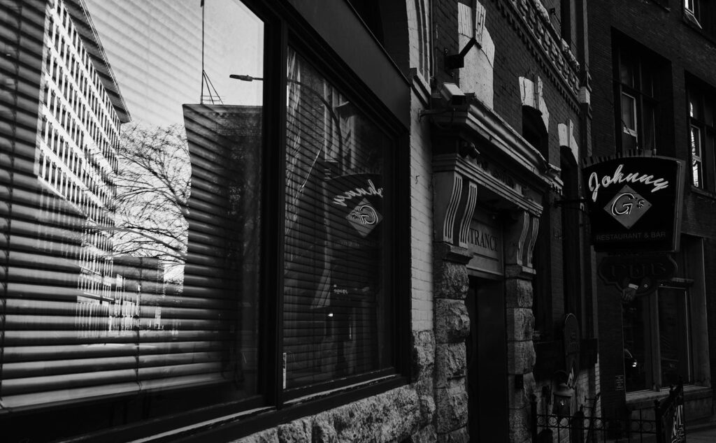 Storefront windows reflecting a building, with a neon sign above the door
