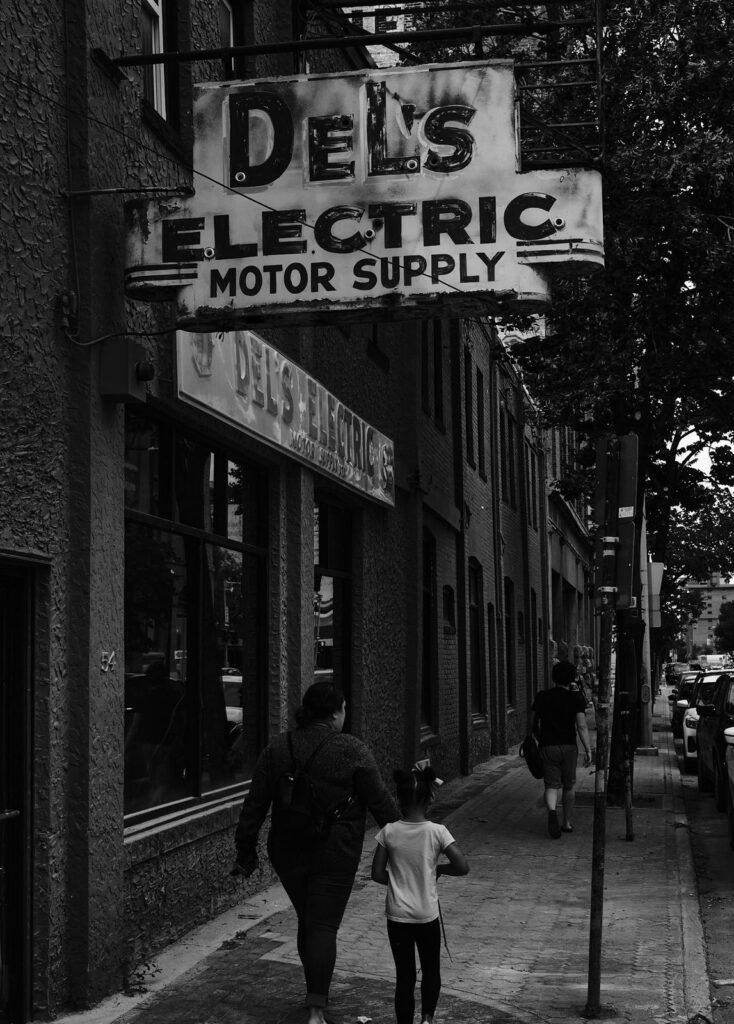 Two pedestrians walking beneath a vintage motor supply sign