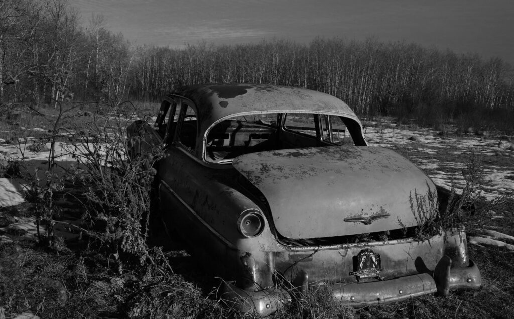 Rusting vintage car abandoned among bushes in a snowy field