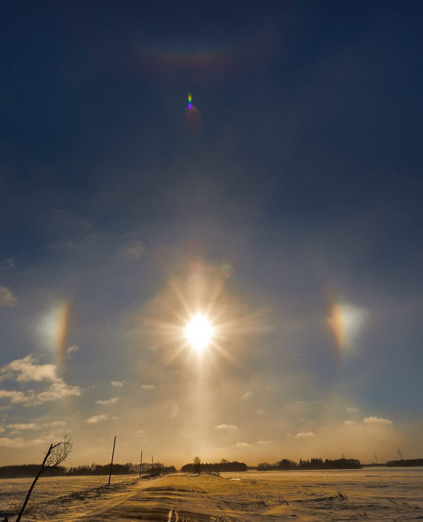 Bright winter sun with sun dogs and a light pillar over a snowy prairie road