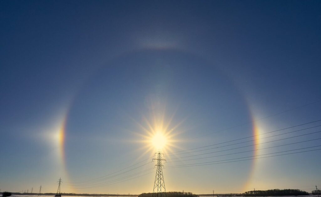 Large halo and sun dogs around the sun behind a power line tower