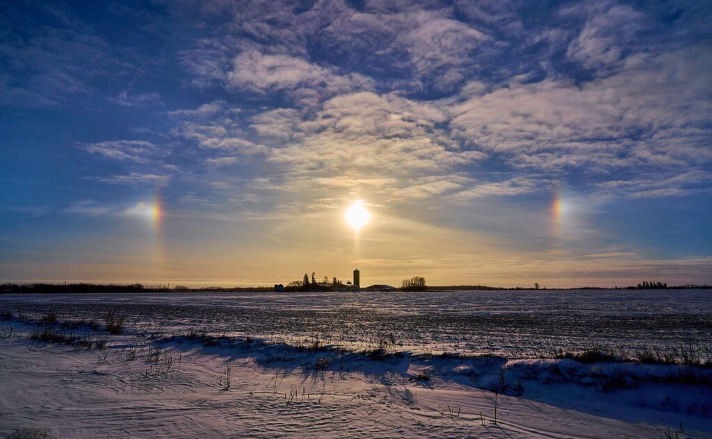 Sun dogs on either side of the sun above a snowy prairie horizon