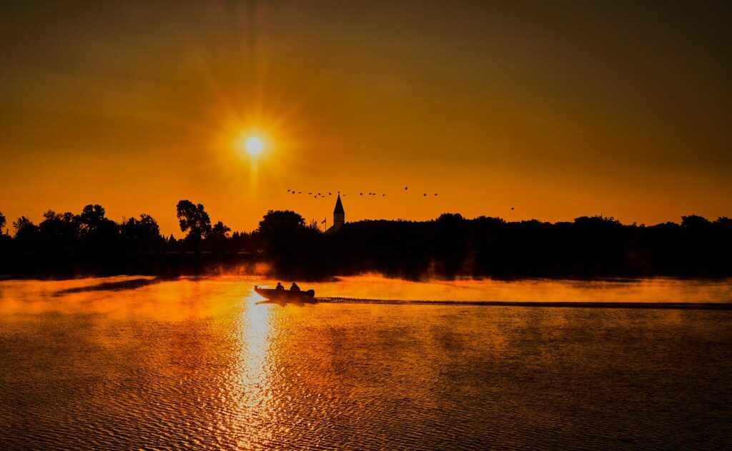 Sunrise over a misty river with a fishing boat and church spire