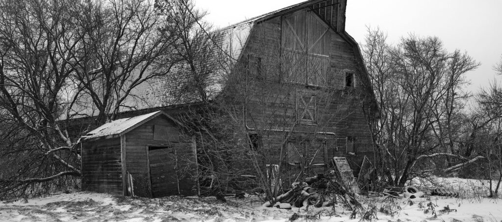 Old barn and shed in the snow among bare trees