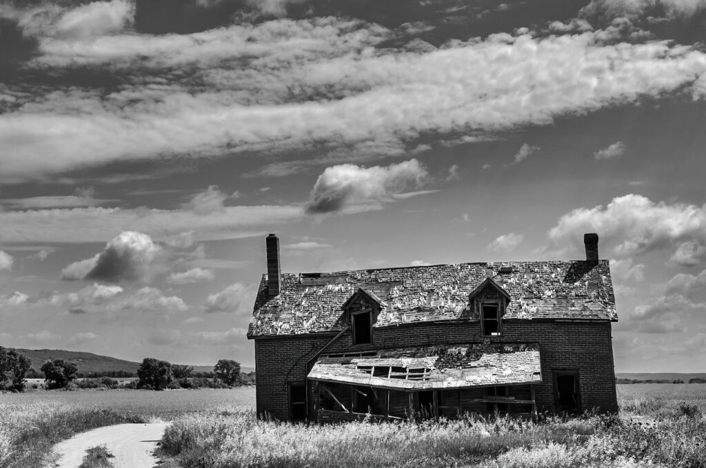 Sagging farmhouse with a collapsed roof on the prairie