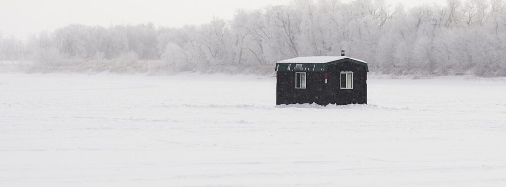 Black ice-fishing shack on a frozen lake with frosted trees