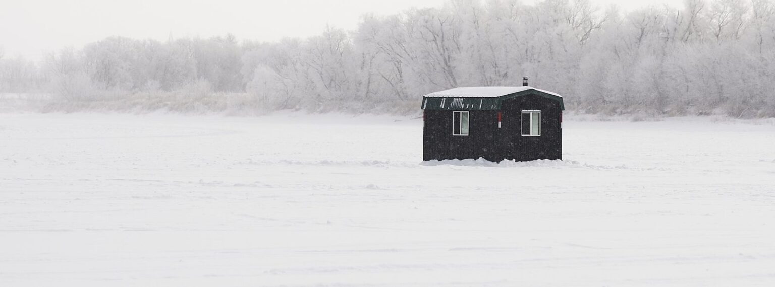 Black ice-fishing shack on a frozen lake with frosted trees